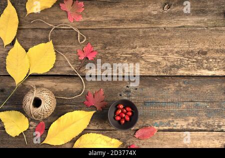 Rosehip in a Cup, autumn leaves and a ball of thread on a natural wooden background. Stock Photo