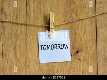 White paper with text 'tomorrow', clip on wood clothespin. Beautiful wooden background. Business concept. Copy space. Stock Photo