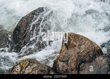 Full frame nature background with boulders in water riffle of mountain river. Powerful water stream of mountain creek. Textured backdrop of fast flow Stock Photo
