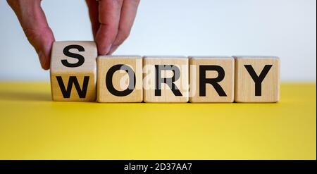 Sorry to worry. Hand turns a cube and changes the word 'worry' to 'sorry'. Beautiful yellow table, white background. Business concept, copy space. Stock Photo