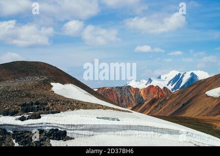 Wonderful view to small glacier on stony hill under blue sky with clouds. Beautiful alpine landscape with ice cornice on rock. Colorful mountain scene Stock Photo