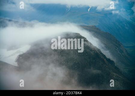 Atmospheric minimalist alpine landscape to giant low cloud among rocky mountain with snow. Low clouds among rockies in valley. Wonderful tranquil high Stock Photo