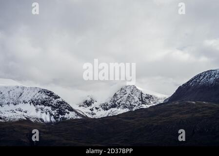 Great black mountains with white snow on tops and glaciers. Dramatic landscape with snowy mountains under cloudy gray sky. Atmospheric alpine scenery Stock Photo