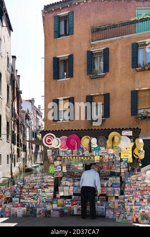 Man searches for magazines, newspapers or souvenirs in a kiosk in front of a facade next to a canal in Venice on a sunny day Stock Photo