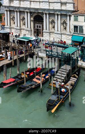 Decorated gondolas are docked between wooden poles in a water canal with a typical Venetian facade in background. Drone view Stock Photo