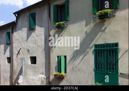 Green door and windows with harsh drop shadows in an old dilapidated gray plastered wall on a street somewhere in sunny Italy Stock Photo