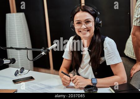 Portrait of happy young female radio host smiling at camera while broadcasting in studio Stock Photo