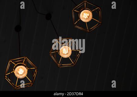 Spider type of ceiling chandelier fragment with hanging bulb lamps over dark background, yellow LED lighting elements Stock Photo