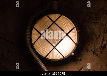 Industrial round light mounted on concrete wall glowing in dark, close-up photo with selective focus Stock Photo