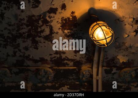 Retro industrial light with tungsten lamp mounted on grunge metal wall glowing in dark, close-up photo with selective focus Stock Photo