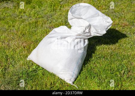 Half-empty white polypropylene bulk bag lays on green grass at sunny day Stock Photo