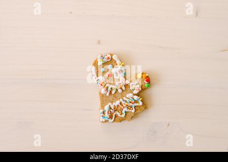 Partially eaten gingerbread man. Gingerbread in the shape of a man - without legs and arms. On a white painted wood texture. Stock Photo