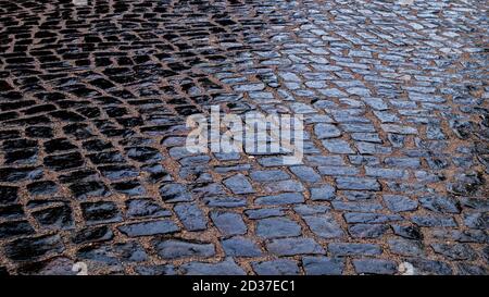 Wet pavement paved with large cobblestones on sandy base in evening in cloudy weather is shiny after rain. Natural background from of road surface. Stock Photo