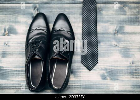 Black leather mens shoes with a black tie with white polka dots on a gray wooden texture. Stock Photo