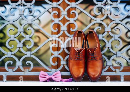 New brown men's shoes and a bow tie with an untied ribbon on the window at the metal grille outside. Stock Photo