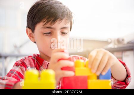 Cute children boy playing in terrace building blocks with face mask protection. Self isolation from covid-19 virus Stock Photo