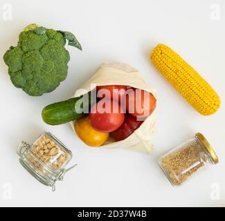 Vegetables in eco bag and nuts in a glass jar on gray surface. Pepper, tomato, corn, cucumber, broccoli in reusable shopping eco friendly cotton Stock Photo