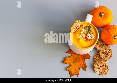 Pumpkin cream soup with seeds and cream in ceramic mug and multigrain healthy crackers on light blue background. Stock Photo