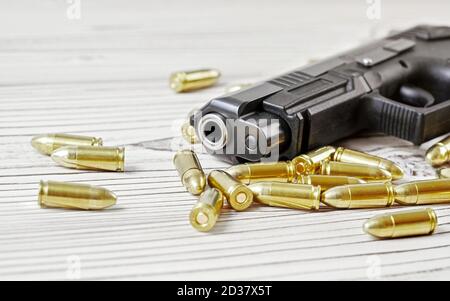 Closeup of modern dark gray gun with yellow brass bullets next to it on white wooden boards Stock Photo