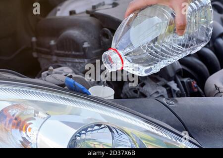 Man pouring distilled water (ecological alternative to washing fluid) to washer tank in car, detail on hand holding clear plastic bottle Stock Photo