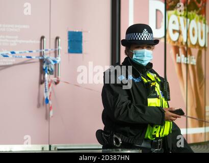 Young female West Midlands Police constable wearing a face mask guards a crime scene in Birmingham, UK.