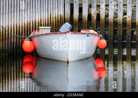 St. John's, Newfoundland / Canada October 2020: A white wooden fishing boat moored with multiple buoys, outboard motor and red trim around the top. Stock Photo