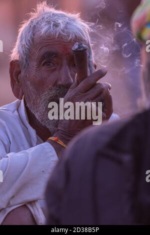 High dynamic range image of a rural Indian man siting an smoking tobacco inside a pipe at Pushkar, Rajasthan, India on 19 November 2018 Stock Photo