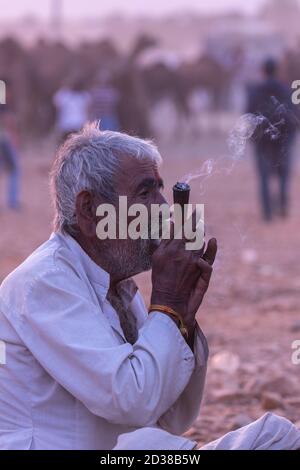 High dynamic range image of a rural Indian man siting an smoking tobacco inside a pipe at Pushkar, Rajasthan, India on 19 November 2018 Stock Photo