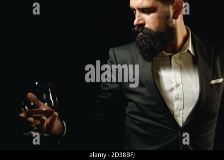 Bearded handsome man holding glass of cognac. Tasting and degustation concept. Barman or Bartender serves cognac. Stock Photo