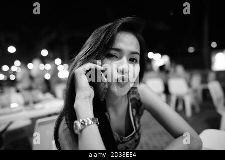 Close up of young beautiful Asian woman talking on mobile phone while puckering her lips at the night market Stock Photo