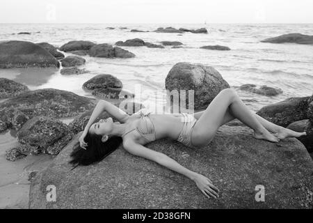 Profile view of young beautiful Asian woman lying down with eyes closed on the rocks of public beach in Hua Hin Thailand Stock Photo