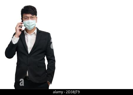 Asian businessman wearing surgical face mask in formal black suit jacket, using smart phone to talking by right hand, look at the camera, studio light Stock Photo