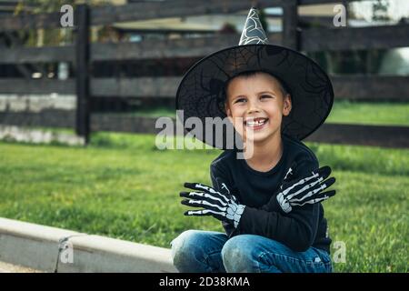 The boy in costumer hat and gloves sitting on the street. Happy halloween. Halloween kids. Stock Photo