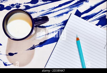 Blue mug with milk on blue-white cotton background , opened notebook with pencil in the background , Stock Photo