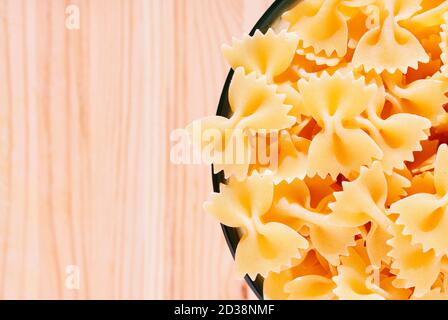 Dry pasta farfalle in glass bowl on wooden table , bow-tie pasta or butterfly pasta with two ruffled edges and the centre pinched together Stock Photo
