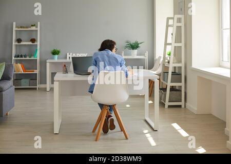 Hard-working business lady writing in notebook and using computer sitting at desk in home office Stock Photo