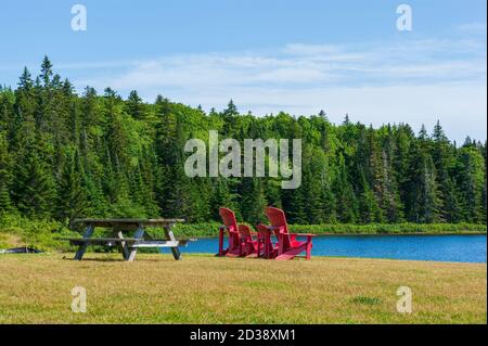 Picnic table and assortment of four red Adirondack chairs at a lookout point on the shore of Wolfe Lake, in Fundy National Park, New Brunswick, Canada Stock Photo