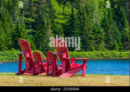 Assortment of four red Adirondack chairs at a lookout point on the shore of Wolfe Lake, in Fundy National Park, New Brunswick, Canada. Stock Photo