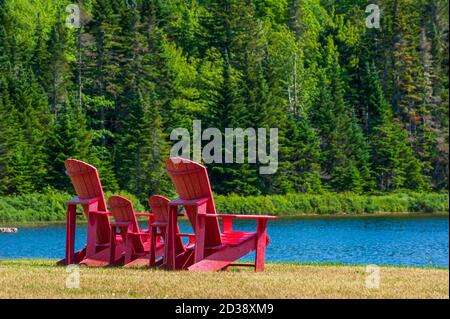 Assortment of four red Adirondack chairs at a lookout point on the shore of Wolfe Lake, in Fundy National Park, New Brunswick, Canada. Stock Photo