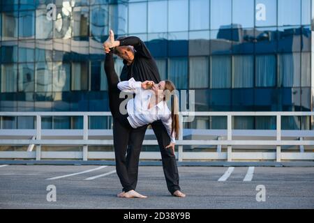 Flexible female make acro yoga element, stretching with male base partner while talk by mobile phone at urban background, sport and business Stock Photo