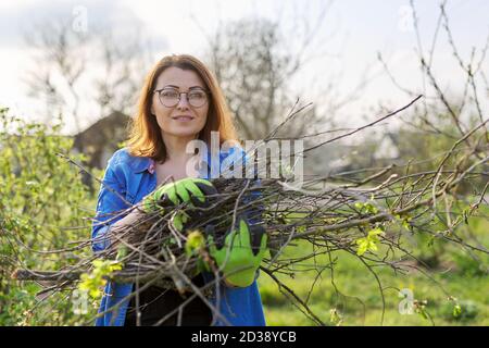 Woman gardener in gloves with dry branches of bushes and fruit trees Stock Photo