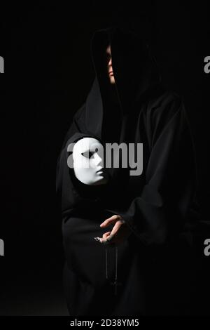 Rite of deal with devil. Sinner in black clothes and demon in sleeve. Man possessed by devil. Evil sorcerer talking with mask. Schizo speaks to himsel Stock Photo