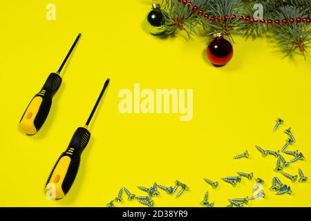 Screws and a screwdriver on a yellow background with a spruce branch. New year banner for hardware store and construction Stock Photo