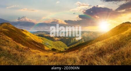 mountain landscape in autumn at sunset. dry colorful grass on the hills. ridge behind the distant valley in evening light. view from the top of a hill Stock Photo