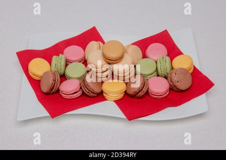 Closeup of colorful french macaroons are beautiful arranged on a white plate on a bright glittering background. Pastries, desserts and sweets. Stock Photo