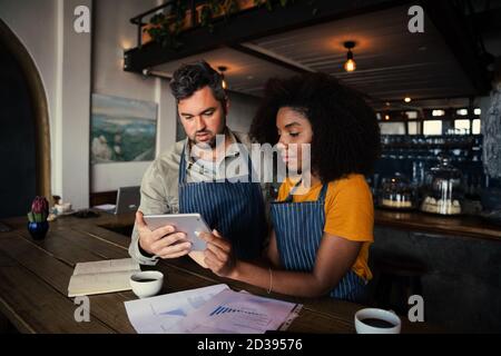 Concerned male and female coffee shop owners scrolling on tablet in rustic coffee shop. Stock Photo