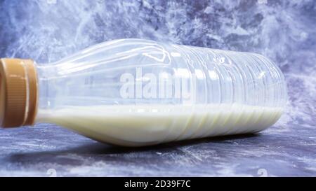 A semi-empty plastic bottle of fresh regular milk lies on a dark gray marble or concrete backdrop. Close-up front view. World milk day concept. Nutrie Stock Photo