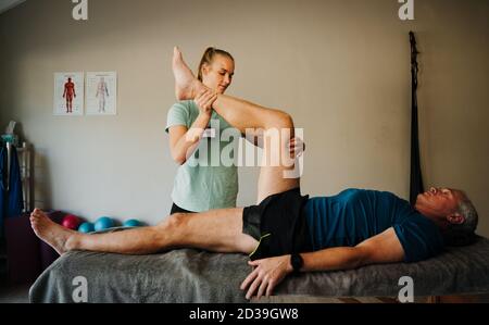 Caucasian female physiotherapist diagnosing male patients knee injury on massage bed, recovering and rehabilitation Stock Photo