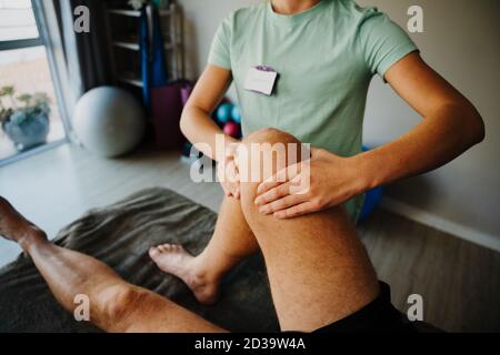 Female therapist treating injured knee of male athlete patient in clinic, sport physical therapy, rehab and recovery Stock Photo
