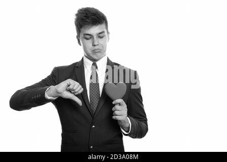 Young sad businessman giving thumb down while holding and looking at red heart ready for Valentine's day Stock Photo